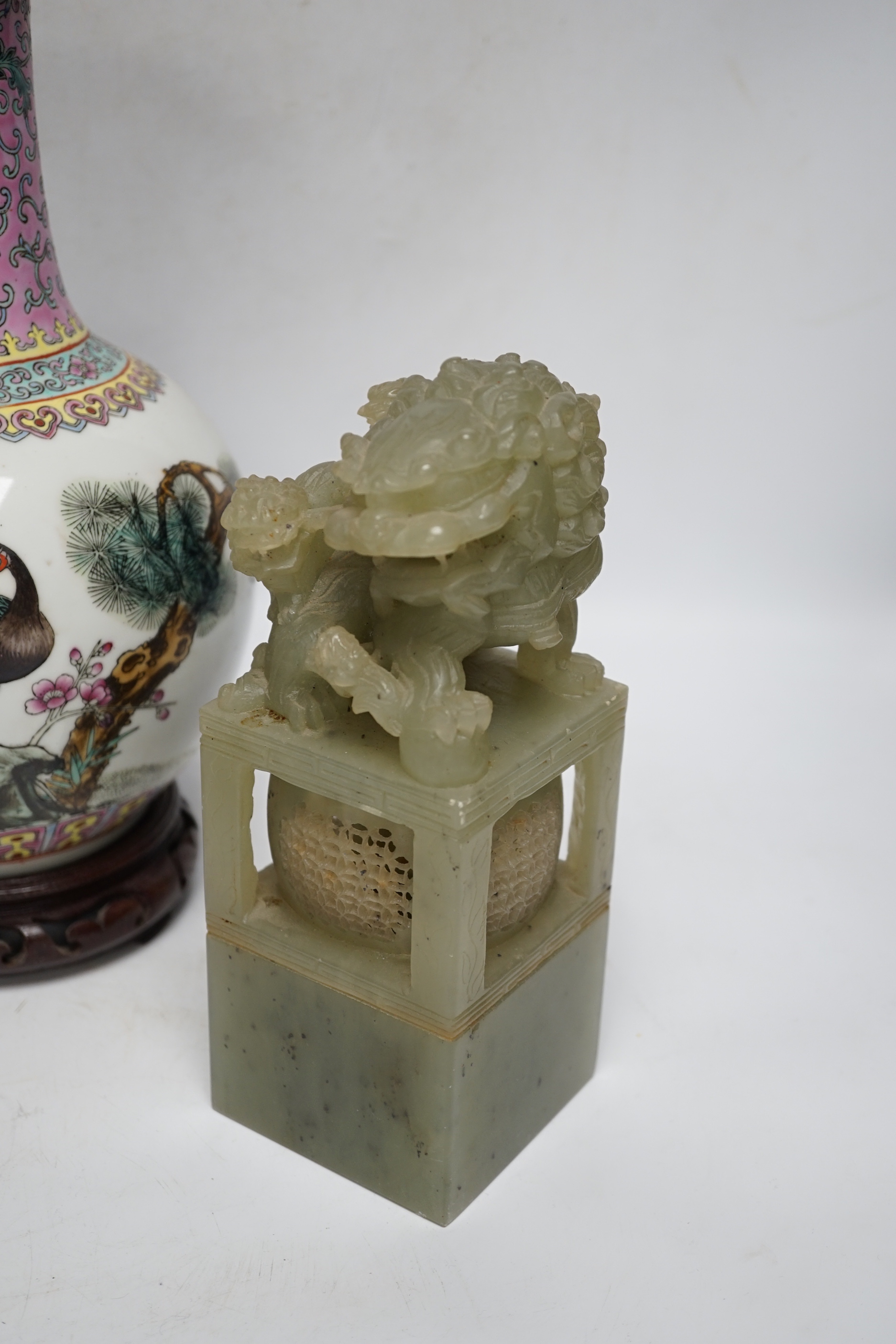 A pair of large Chinese soapstone ‘Temple Guardian lion’ seals, 21cm, and a Chinese famille rose vase, 27cm, on carved wood stand